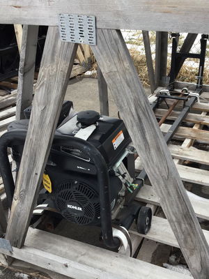 Small engine or motor on a wooden pallet with a wooden frame structure in the background.