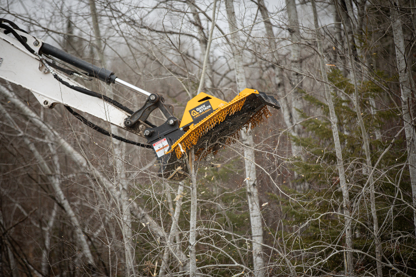 Mower attachment cutting a tree in a forest setting