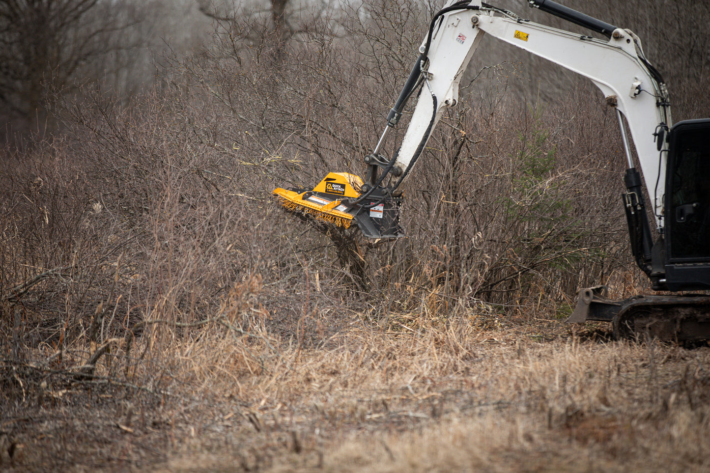Excavator with a brush cutter attachment clearing brush in a wooded area