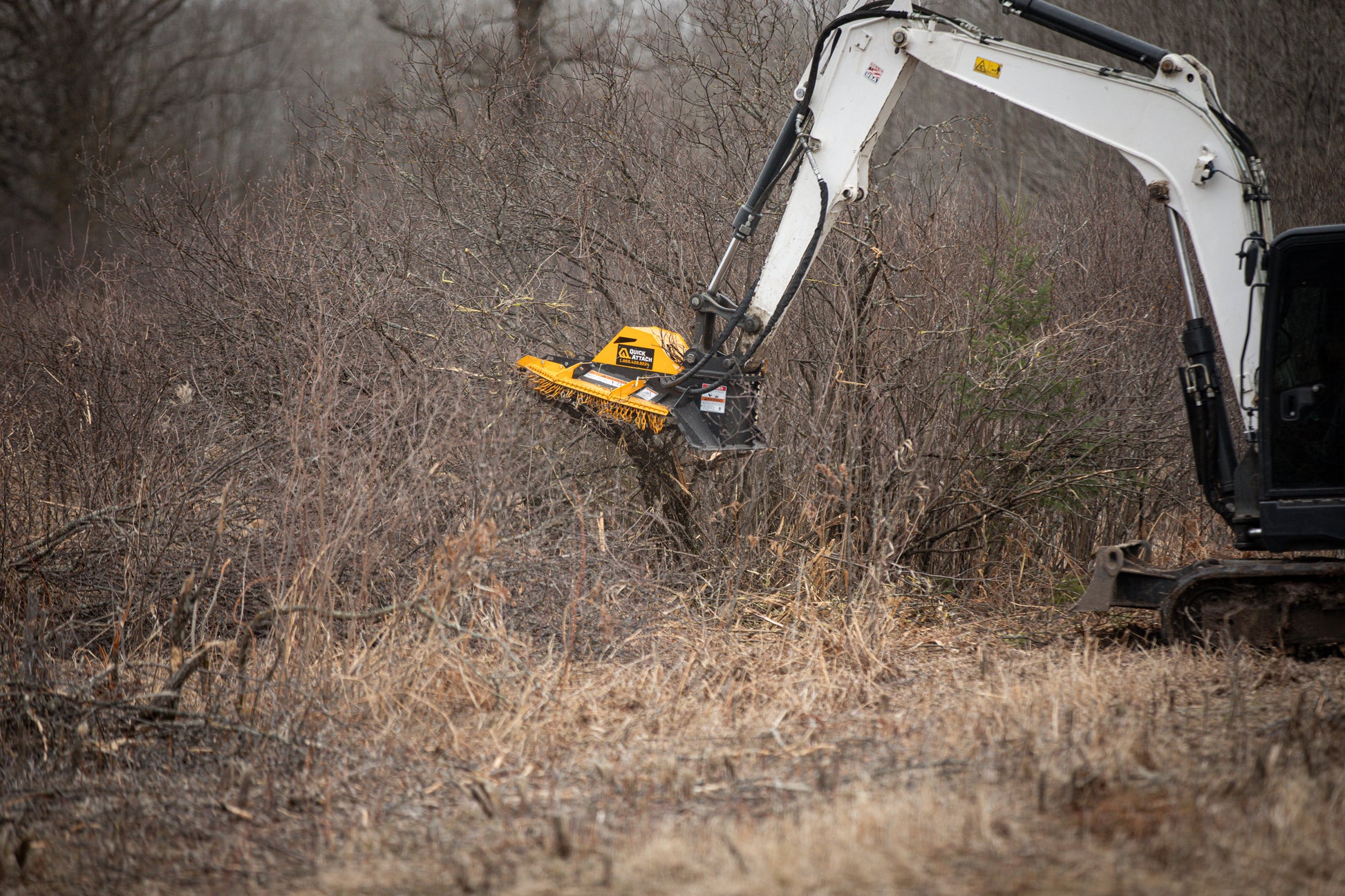 Excavator with a brush cutter attachment clearing brush in a wooded area