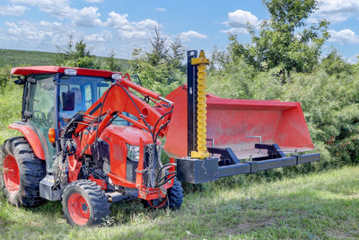Bucket Mount Limb Cutter attached to a red tractor in a grassy field.