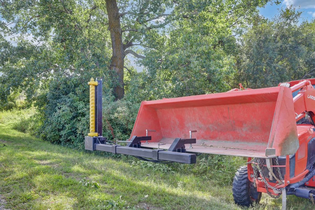 Side view of the Bucket Mount Limb Cutter on a red tractor near a wooded area.