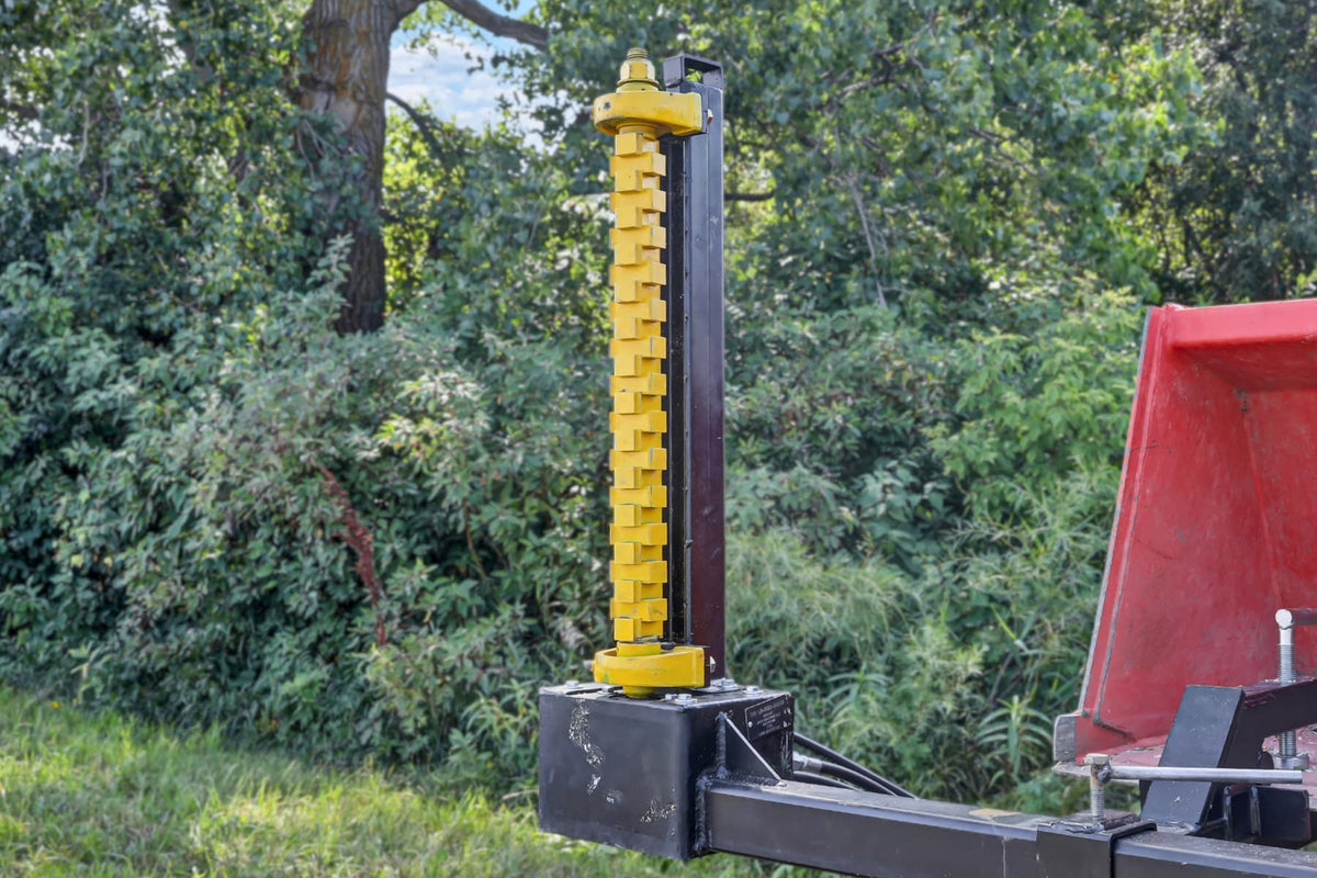 Closer view of the Bucket Mount Limb Cutter’s vertical yellow rotor beside a red tractor.