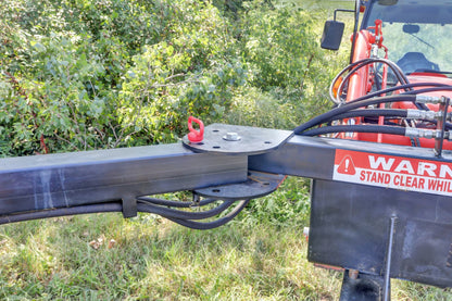 Close-up of the Compact Limb Cutter’s black mounting arm and hydraulic hoses attached to a red tractor beside dense brush.