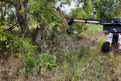 Junior Limb Cutter mounted on a skid steer beside overgrown trees and brush.