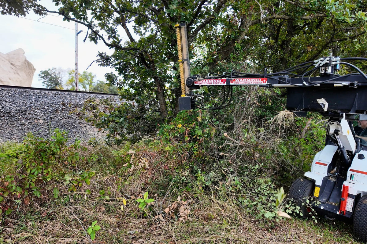 White skid steer using the Junior Limb Cutter near a tree at the edge of a field.