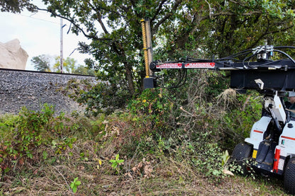 White skid steer using the Junior Limb Cutter near a tree at the edge of a field.