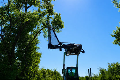 Limb Cutter 6 raised above a tractor on a boom beneath tall trees.