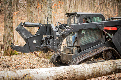 Skid steer loader with attachments cutting through a log in a forest setting