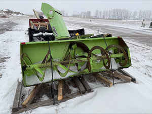 Green snowblower on a wooden platform in a snowy landscape