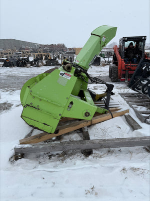 Green piece of construction equipment on a snowy ground with buildings in the background