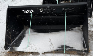 Large black snow plow attached to a vehicle on a snowy road